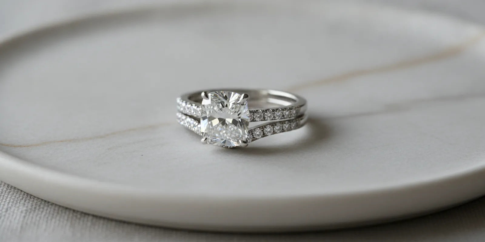 Close view of a diamond engagement ring beside a wedding band on a neutral jewelry display